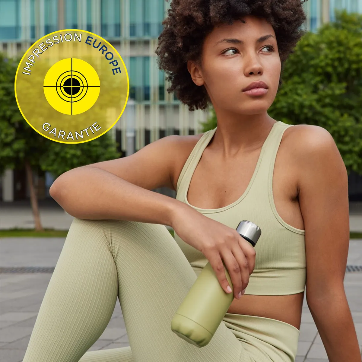 Femme sportive en tenue beige tenant une gourde assortie, avec le logo 'Impression Europe Garantie' en arri